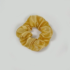 Detailed view of champagne satin silk scrunchie with soft pleated texture and glossy finish