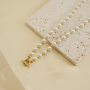 Détail d'un collier de perles blanches et dorées avec fermoir à bascule OT sur pierre