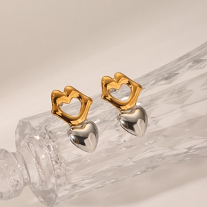 Detail of two-tone gold and silver heart earrings placed on textured glass bottle