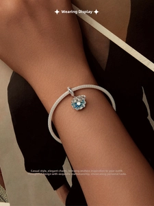 Détail d'un bracelet en maille argentée avec un pendentif fleur émaillé bleu et perle