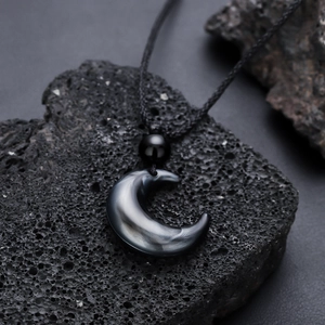 Minimalist crescent moon obsidian pendant on woven cord atop volcanic rock base
