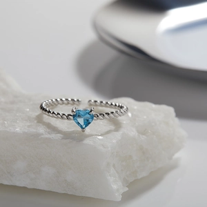 Close-up of S925 silver heart ring with blue topaz gemstone on textured stone surface