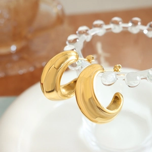 Polished 18k gold plated C-shaped croissant earrings on a glass display stand