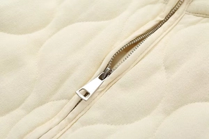 Detailed close-up of the metal zipper and quilted texture on the beige stand collar jacket