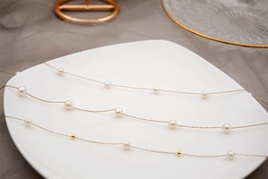 Detail of freshwater pearl gold necklaces on white plate with elegant mesh background