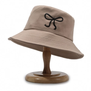 Light khaki cotton bucket hat with black bow embroidery on wooden stand
