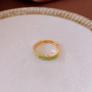 Vue macro d'une bague ouverte dorée avec émail vert et cristaux rouges brillants