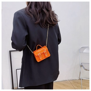 Model wearing a bright orange patent leather crossbody bag with a gold chain strap