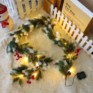 Detail of Christmas pine needle garland with red berries and warm LED lights on soft rug