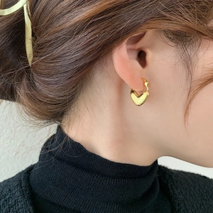 Close-up of minimalist heart-shaped zirconia earrings in 18K gold on a model ear