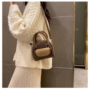 Brown suede crossbody bag with beige plush pocket detail shown on a white sweater