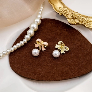 Elegant pink bow pearl earrings with gold finish displayed on a heart-shaped felt pad