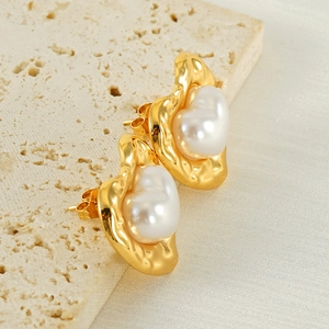 Detail of vintage heart-shaped gold-plated pearl earrings on a beige stone surface