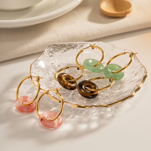 Gold hoop earrings with pink, brown, and green donut stone pendants on a glass tray