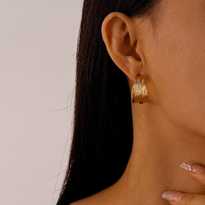 Detail of golden C-shape earrings with textured pleats worn on a female model