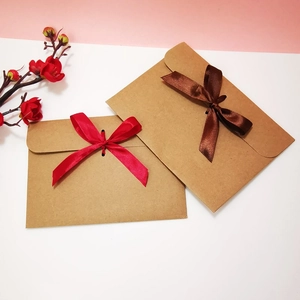 Close-up of vintage kraft paper envelopes with red and coffee ribbon bows and floral accents
