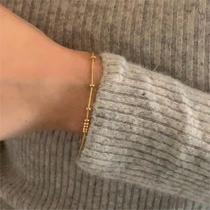 Detail of 925 sterling silver snake chain bracelet with gold beads on a sweater sleeve