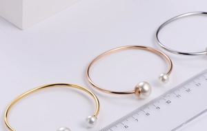 Three-color minimalist pearl cuff bracelets in gold and silver next to a measuring ruler