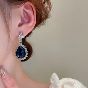 Detail of silver drop earring with deep blue stone and sparkling zircons worn by a model