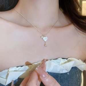 Close-up of a silver heart-shaped shell necklace with small pearls on a female neck