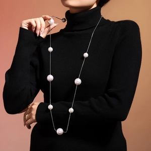 Long collier en acier inoxydable avec grandes perles blanches porté sur un pull noir élégant