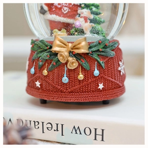 Close-up of red knit texture base with golden bow and bells on Christmas snow globe