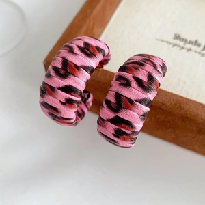 Close-up of pink leopard print C-shape earrings with woven texture and vintage pattern