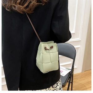 Close-up of hand-woven light green bucket bag with thin shoulder strap on a model