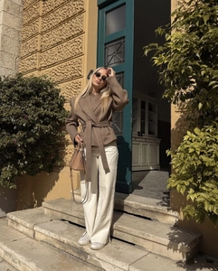 Detail shot of a French-style brown belted wool coat and white wide-leg trousers ensemble