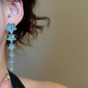 Macro shot of long silver tassel earrings with six blue zircon flowers on a model