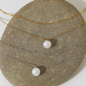 Double-layered gold and silver necklaces with 10mm white pearls on a natural stone