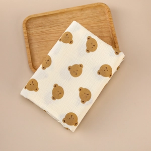 Detail of soft beige cotton muslin swaddle blanket with brown bear prints on wooden tray