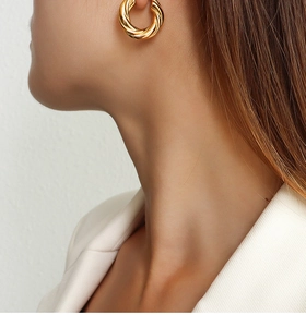 Detail shot of a model wearing a gold twisted croissant hoop earring in 18K plated finish