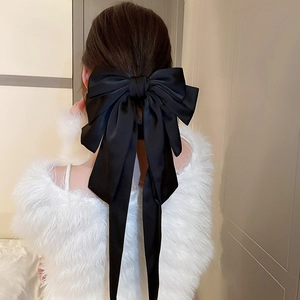 Détail d'une pince à cheveux en satin noir avec de longs rubans sur le modèle