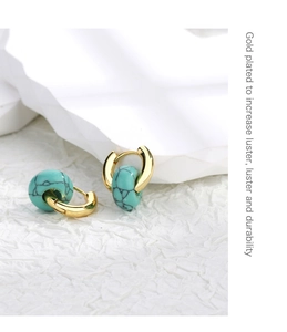 Macro shot of gold plated hoop earrings with turquoise stones on white decor