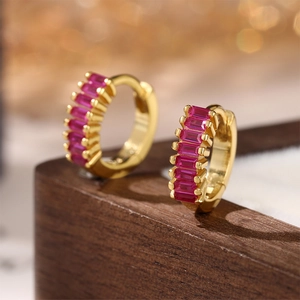 Macro detail of gold hoop earrings with baguette-cut red zircons on display stand
