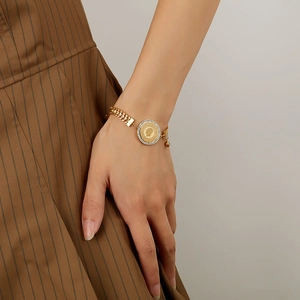 Detail of a gold wheat chain bracelet featuring a rhinestone coin pendant on a wrist