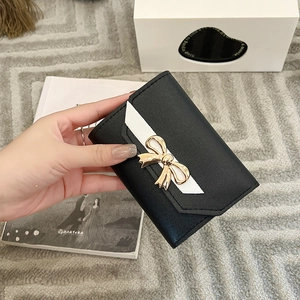 Detailed view of women's short trifold wallet with golden bow and white V-shaped patch