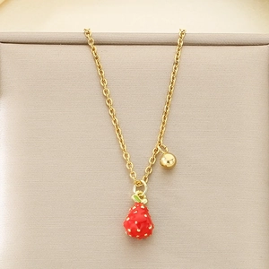 Macro detail of the golden chain necklace featuring a red strawberry pendant and gold bead