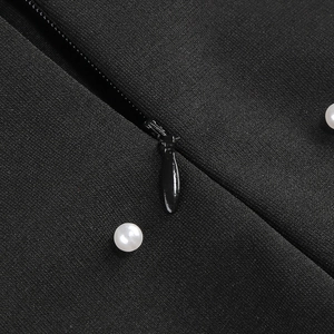 Détail de robe en maille noire avec deux perles blanches et une fermeture éclair invisible