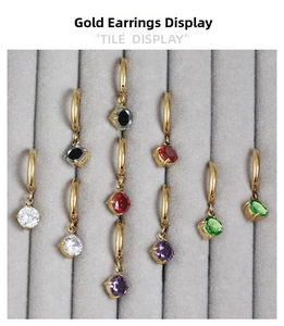 Detailed display of gold hoop earrings with colorful round-cut gemstones on gray velvet