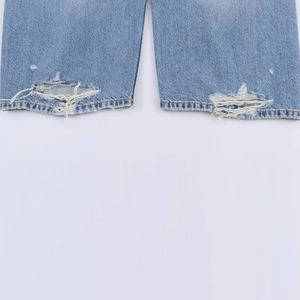 Détail de l'ourlet effiloché et de l'usure sur le jean en denim délavé bleu clair