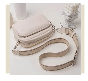 Detail view of cream leather crossbody bag with multi-zipper layers and wide woven strap