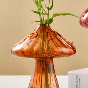 Close-up of mushroom-shaped amber glass vase with textured surface and green plant