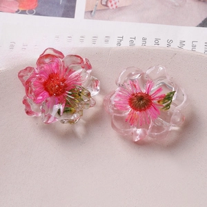 Macro detail of transparent resin charms with embedded real pink dried daisy flowers