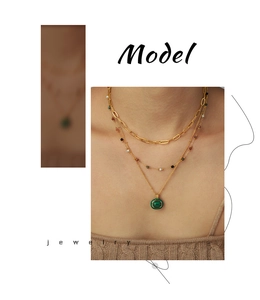 Close-up of triple-layered gold chain necklace with a green oval gemstone pendant on model