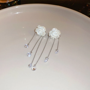 Détails macro des boucles d'oreilles camélia aux pétales 3D et longs pompons argentés