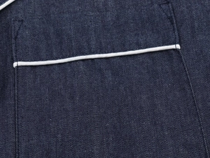 Detail of dark blue denim shirt pocket featuring contrast white piping and twill texture