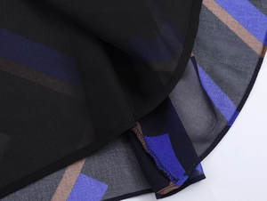 Detail eines schwarzen Chiffon-Midirocks mit blau-braunem Geometriedruck und Saumnaht