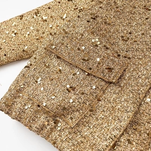 Dettaglio ravvicinato di paillettes dorate su tessuto tweed con trama lucida